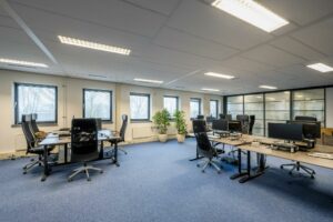 Modern kantoorinterieur aan de Joop Geesinkweg met bureaus, bureaustoelen, computers en grote ramen.